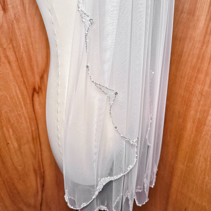 A classic fingertip length wedding veil with a pearl-embellished edge showing a graceful, airy drape.