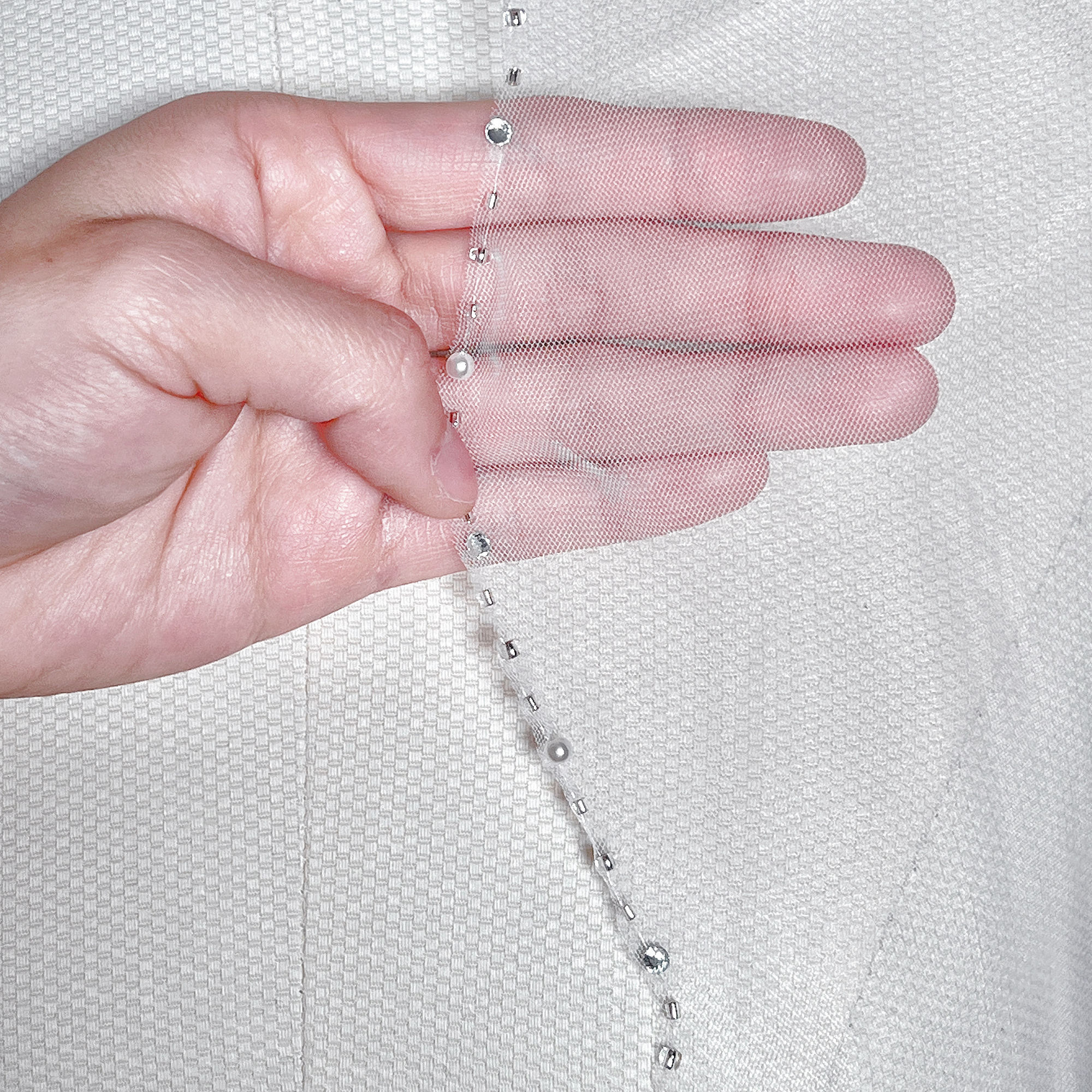 Detailed close-up of the delicate silver beading and embroidery along the scalloped trim of a bridal veil.