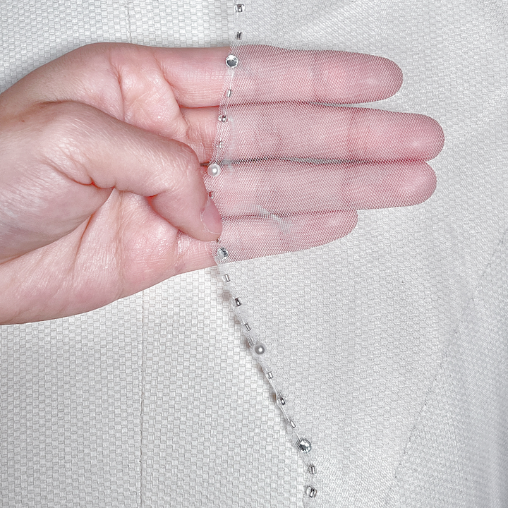 Detailed close-up of the delicate silver beading and embroidery along the scalloped trim of a bridal veil.