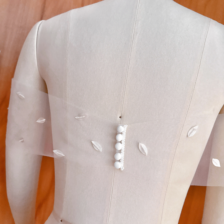 A macro close-up image showing the fine textures of the hand-sculpted silk petals and the meticulous placement of white glass seed beads on the sheer wrap tulle.