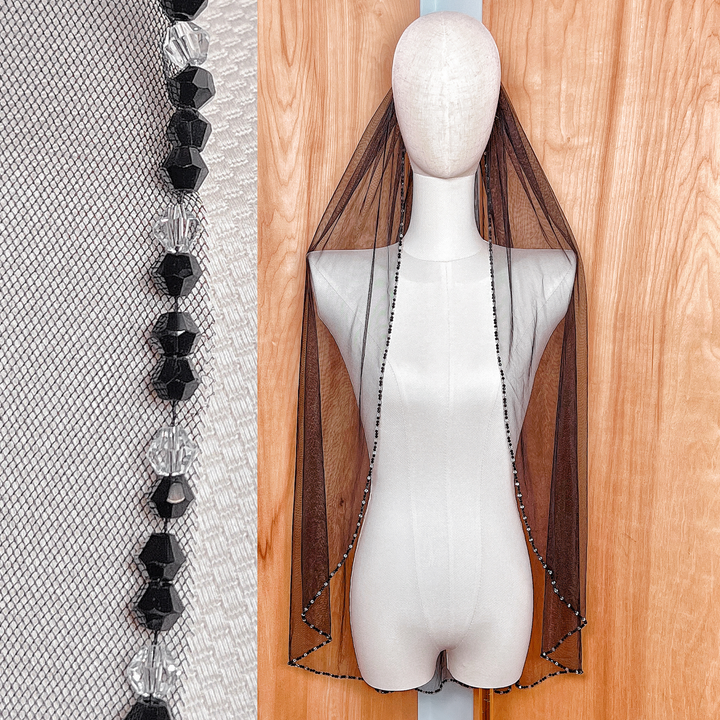 Fingertip length black wedding veil with a detailed crystal beaded edge shown on a bridal display.
