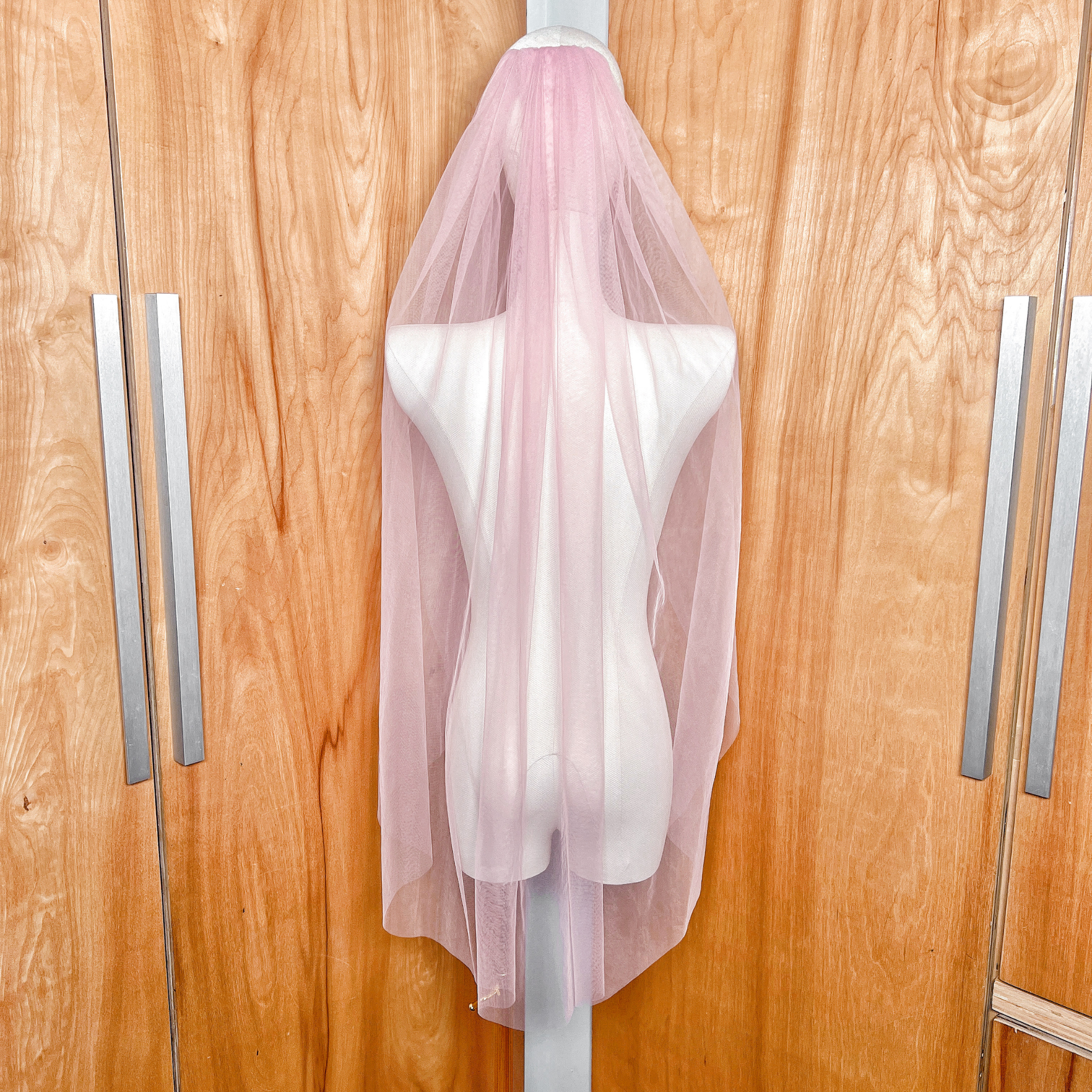Rear view of a soft blush pink wedding veil in fingertip length, showing the sheer tulle fabric and elegant drape.