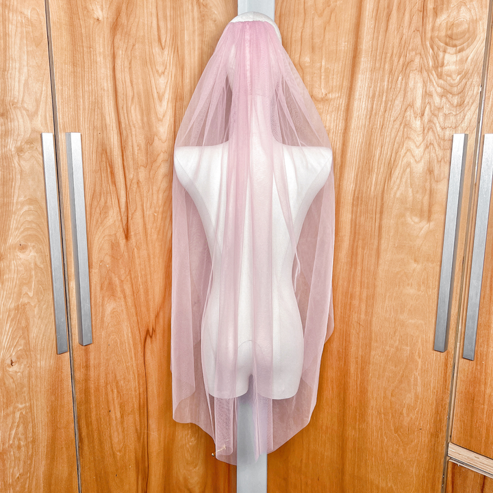 Rear view of a soft blush pink wedding veil in fingertip length, showing the sheer tulle fabric and elegant drape.