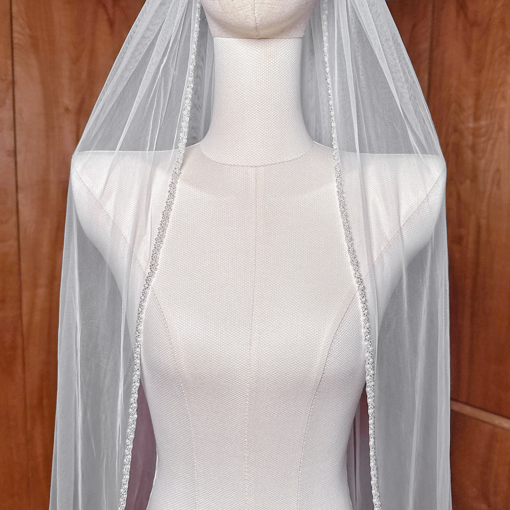 Elegant cathedral length bridal veil with a shimmering beaded edge draped over a mannequin.