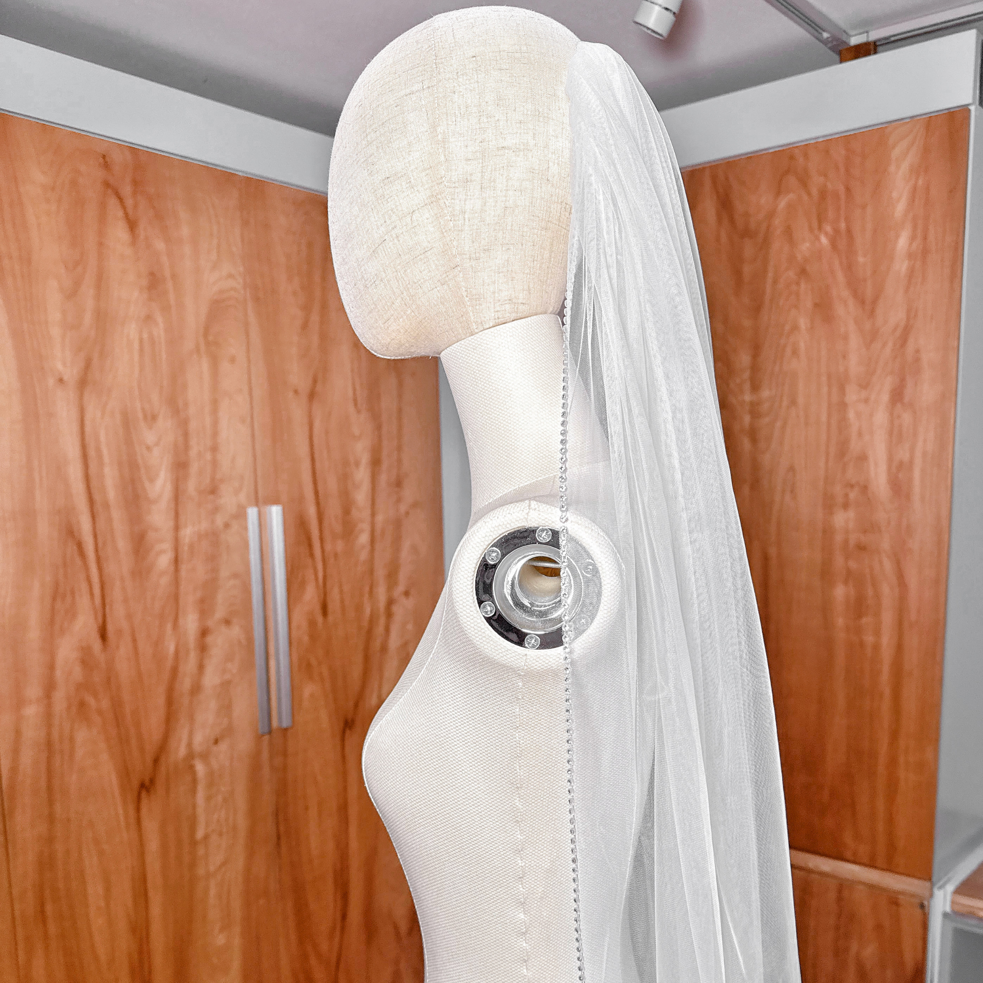 Shimmering rhinestone edge wedding veil in dramatic cathedral length shown on a mannequin bust.