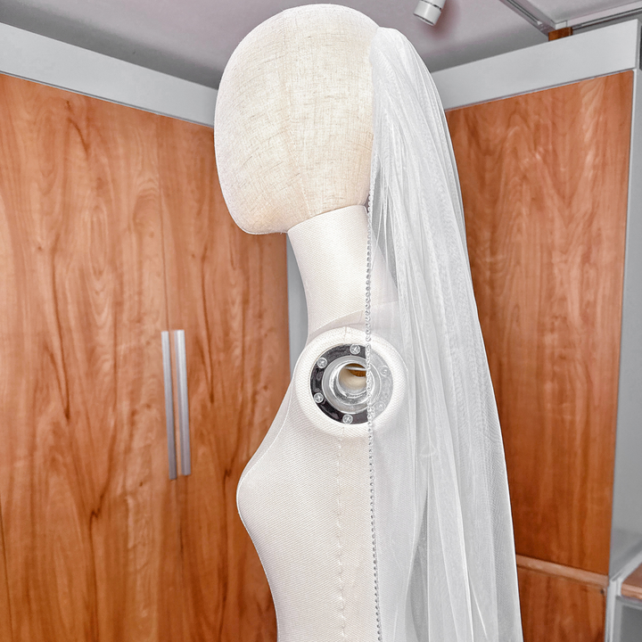 Shimmering rhinestone edge wedding veil in dramatic cathedral length shown on a mannequin bust.