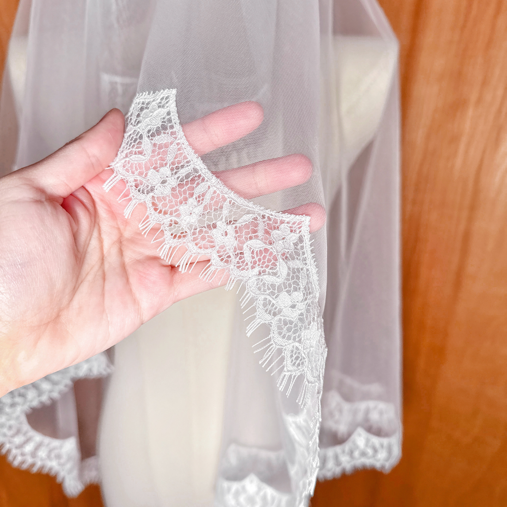 Close-up detail of the floral lace trim on a hip-length drop wedding veil, shown on a professional dress form.