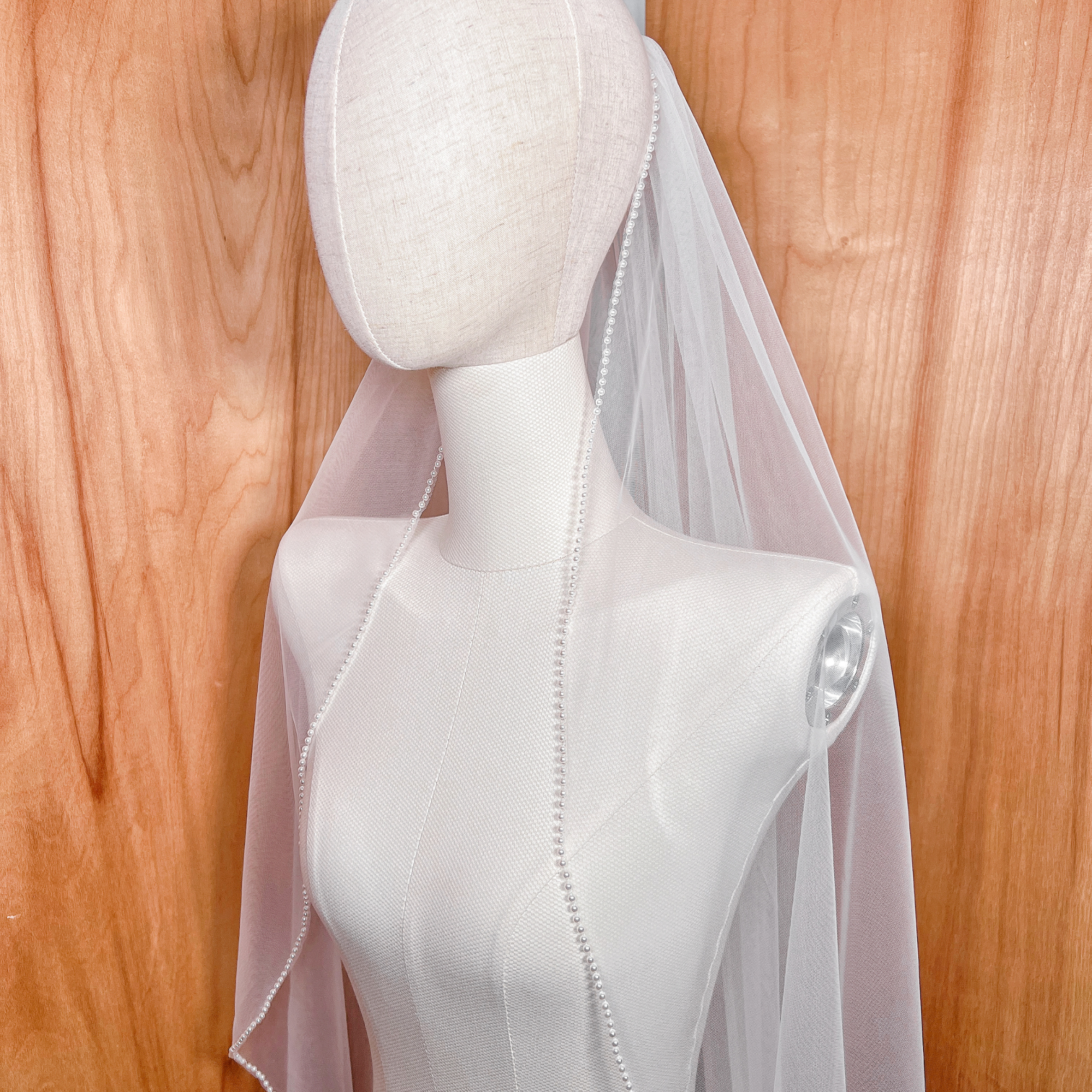 Soft tulle wedding veil with hand-applied cascading pearls along the entire edge, designed in a classic fingertip length.