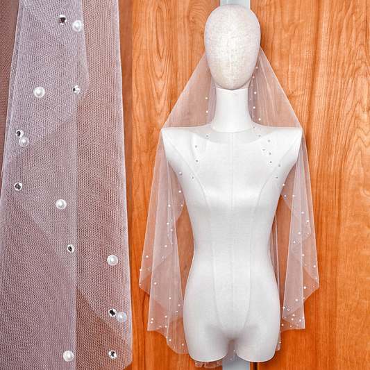 A fingertip length bridal veil with rhinestone and pearl accents, draped to show the sheer fabric and decorative finish.