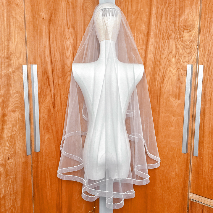 Two-tier fingertip-length bridal veil featuring a structured horsehair trim and delicate pearl embellishments.