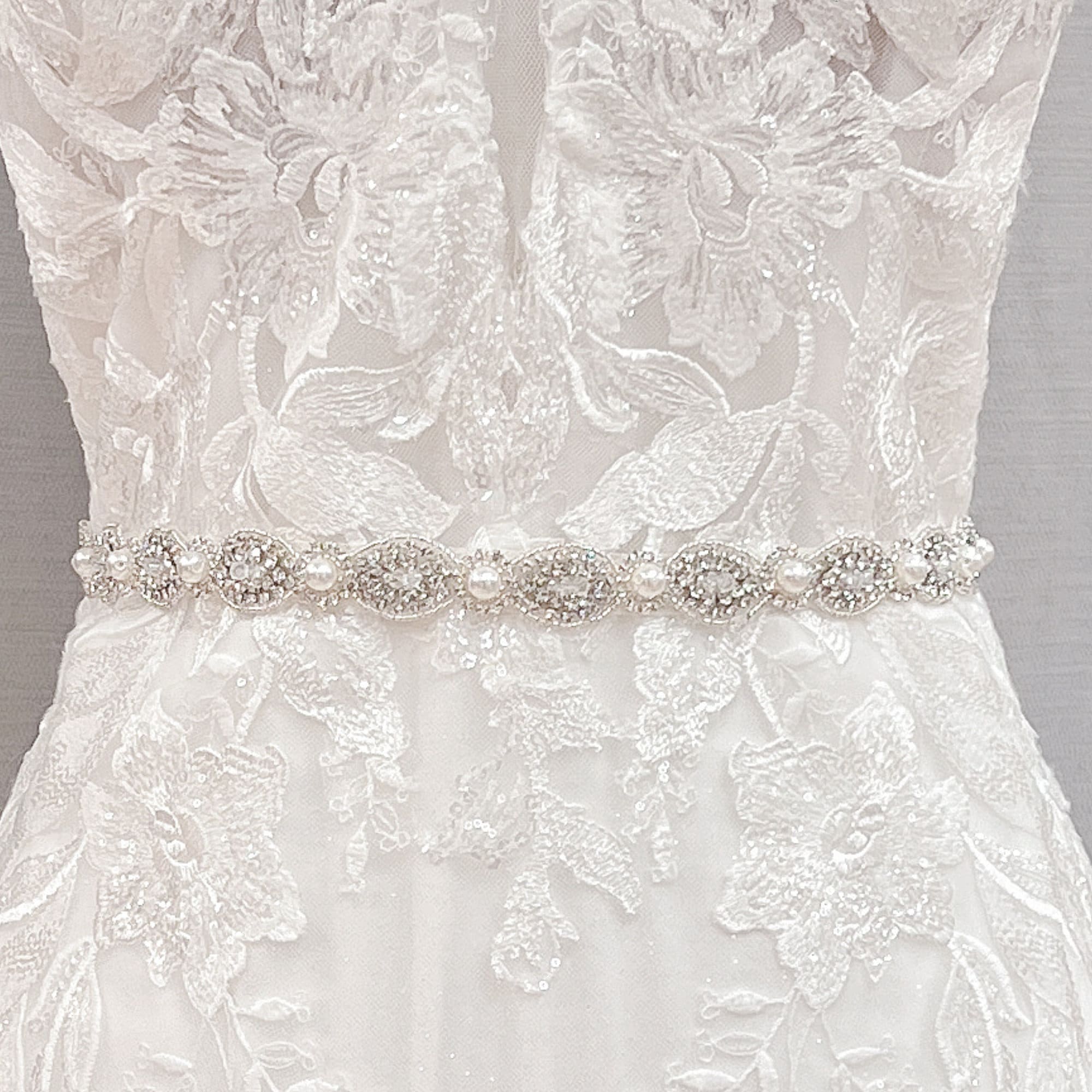 Close up view of a silver rhinestone and pearl bridal belt showcasing the sparkling gemstone pattern.