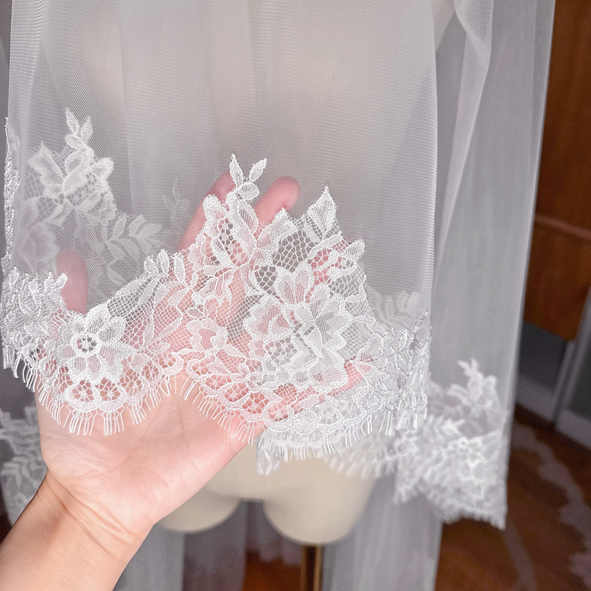 Close-up shot of the fine Chantilly lace detail on a two tier cathedral length wedding veil draped over a dress form.