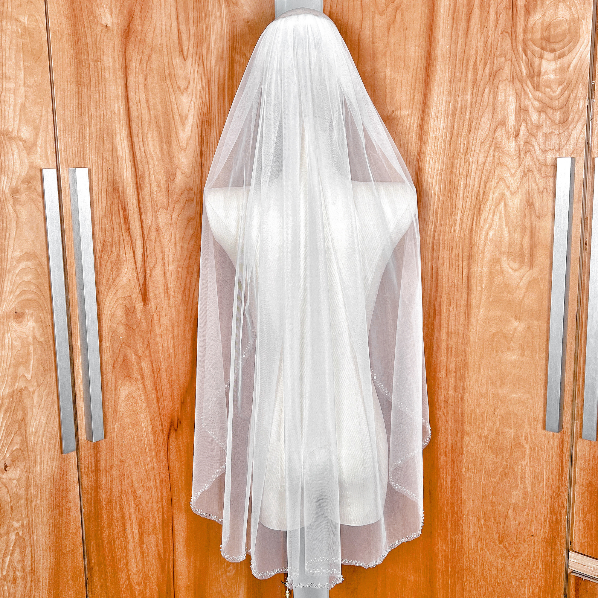 Back view of a fingertip length pearl and crystal beaded edge wedding veil draped on a dress form.