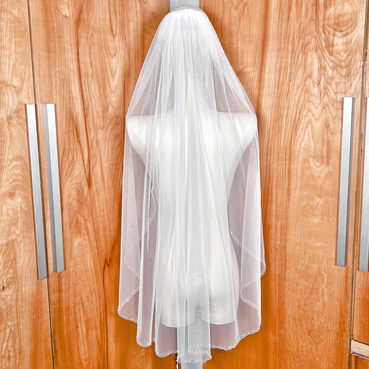 Back view of a fingertip length pearl and crystal beaded edge wedding veil draped on a dress form.