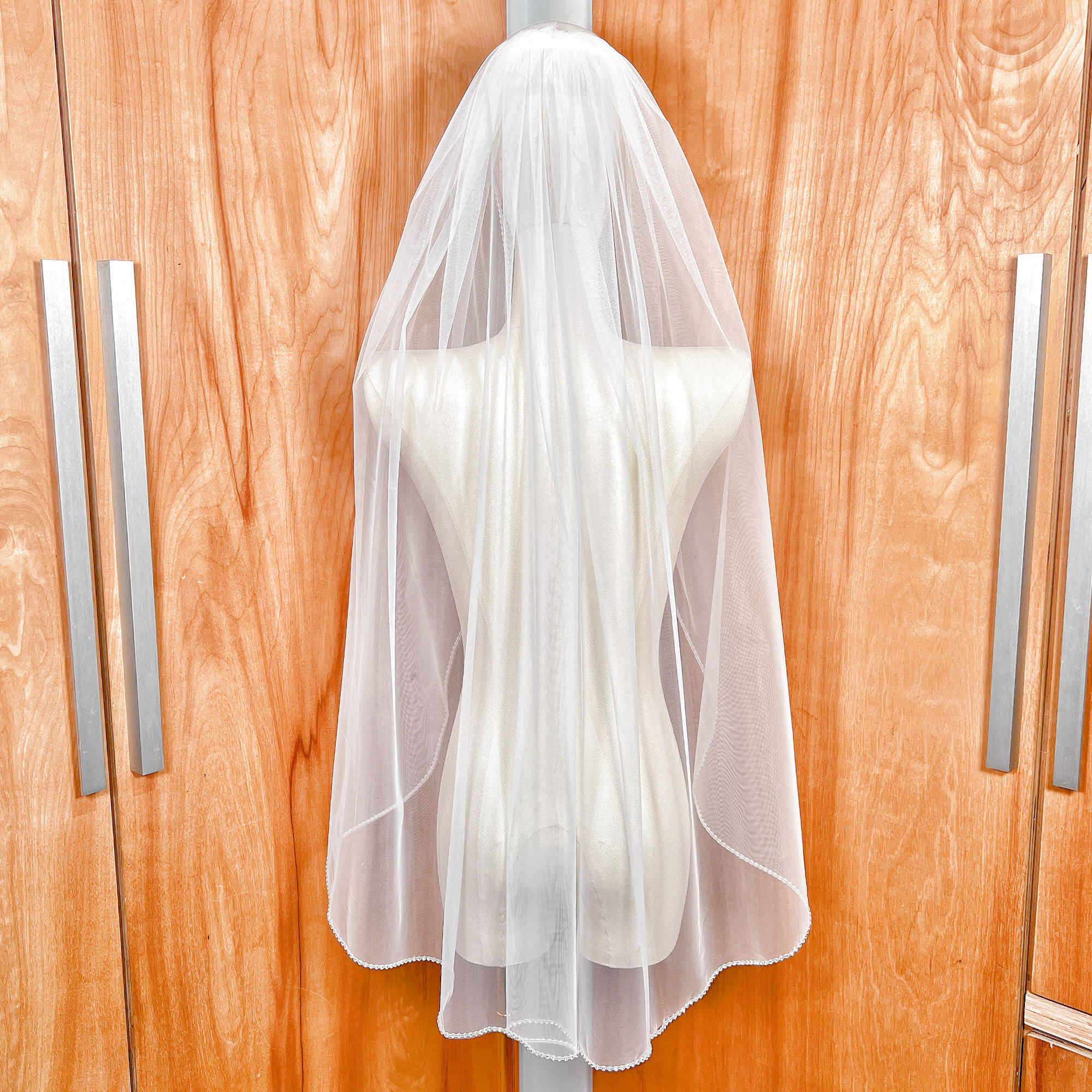 Back view of a sheer fingertip length rhinestone edge wedding veil on a display bust.