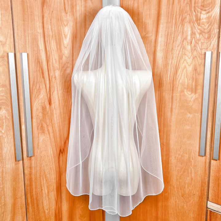 Back view of a sheer fingertip length rhinestone edge wedding veil on a display bust.