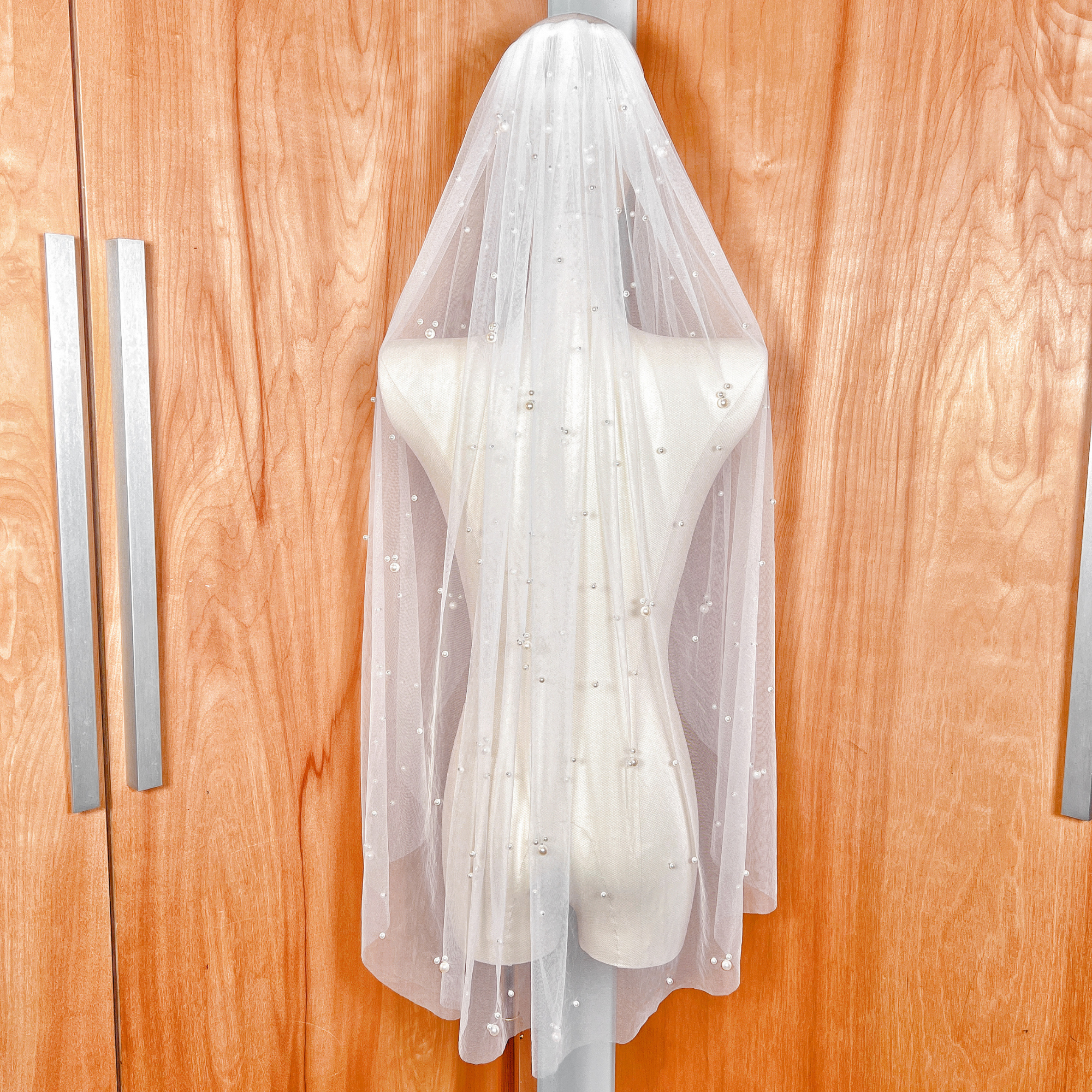 Rear view of a fingertip-length wedding veil with scattered pearls, showcasing how the veil falls gracefully to the fingertips for a classic bridal look.