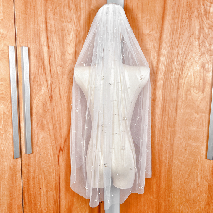 Rear view of a fingertip-length wedding veil with scattered pearls, showcasing how the veil falls gracefully to the fingertips for a classic bridal look.