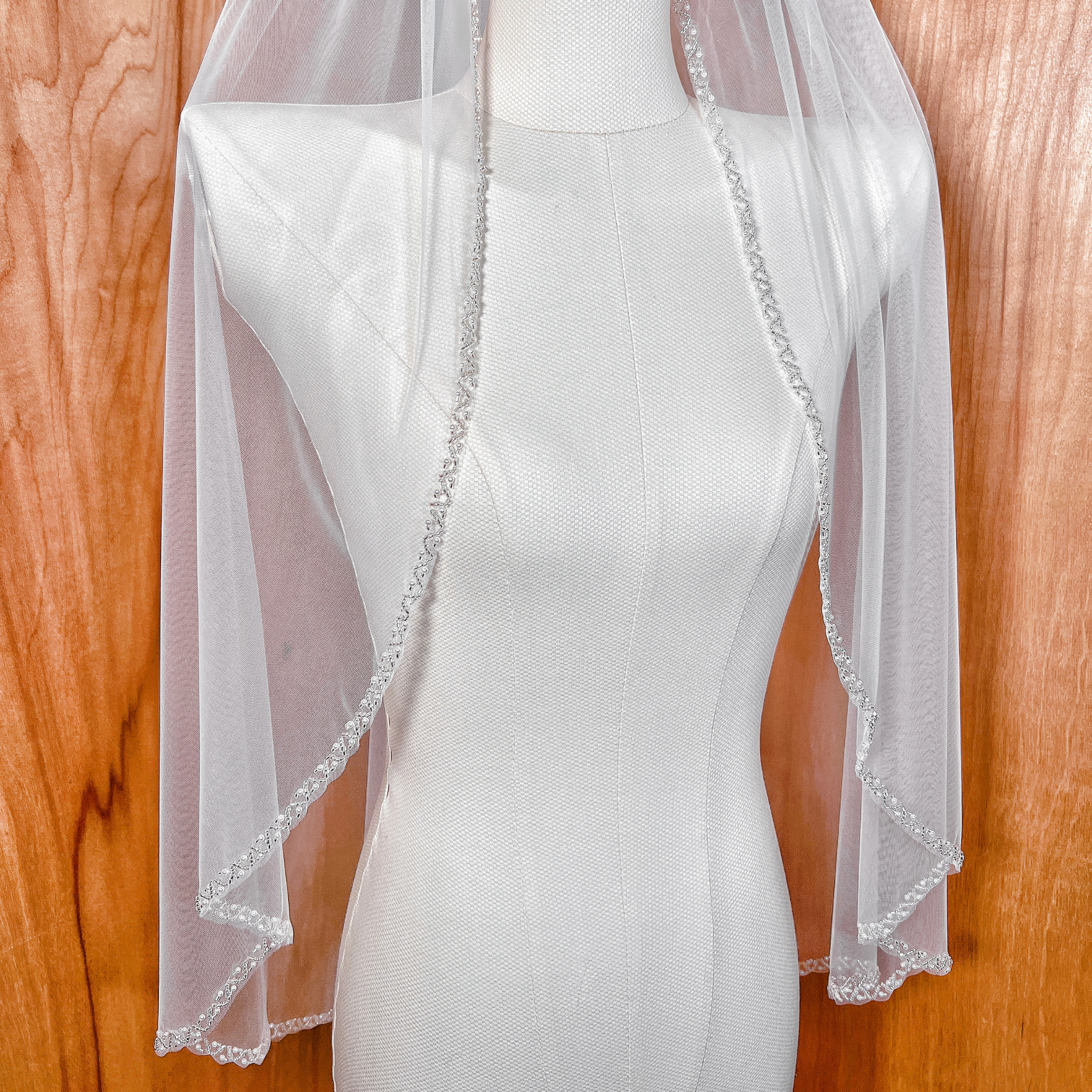 Detailed view of a soft tulle bridal veil featuring an elegant pearl beaded border at fingertip length.