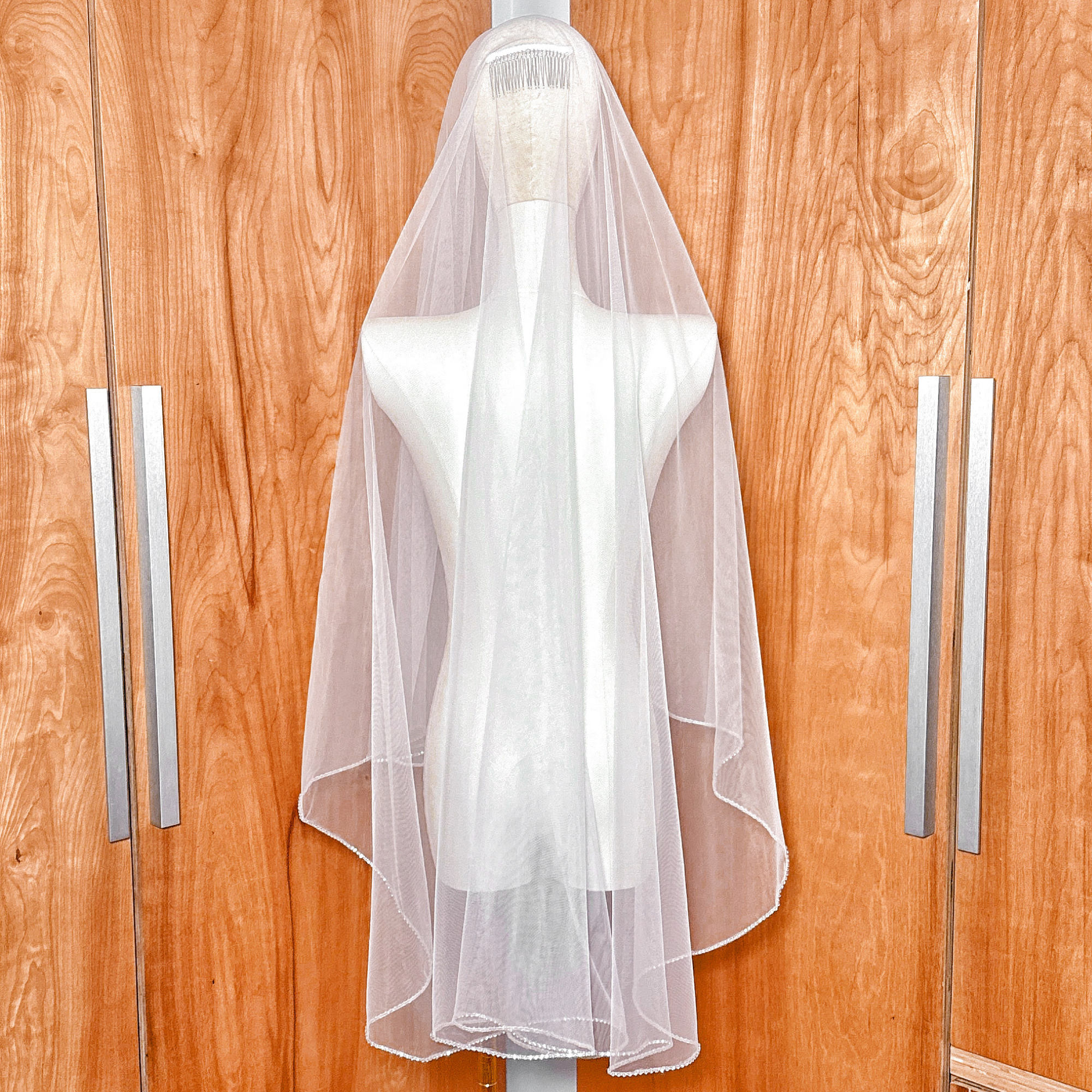 Rear view of a fingertip length two tier wedding veil with shimmering rhinestone edge trim.