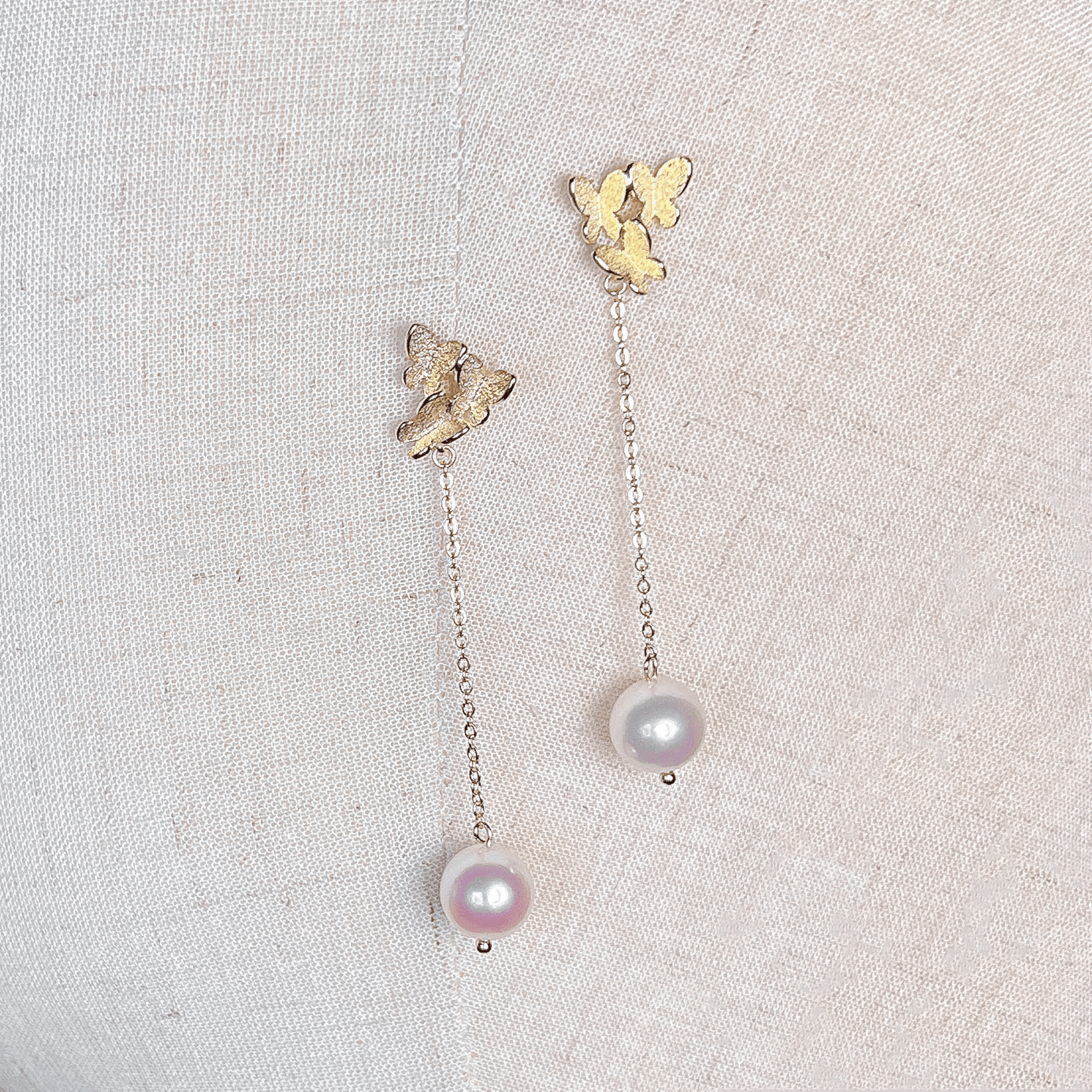 Pair of gold butterfly pearl dangle earrings displayed against a clean white background.