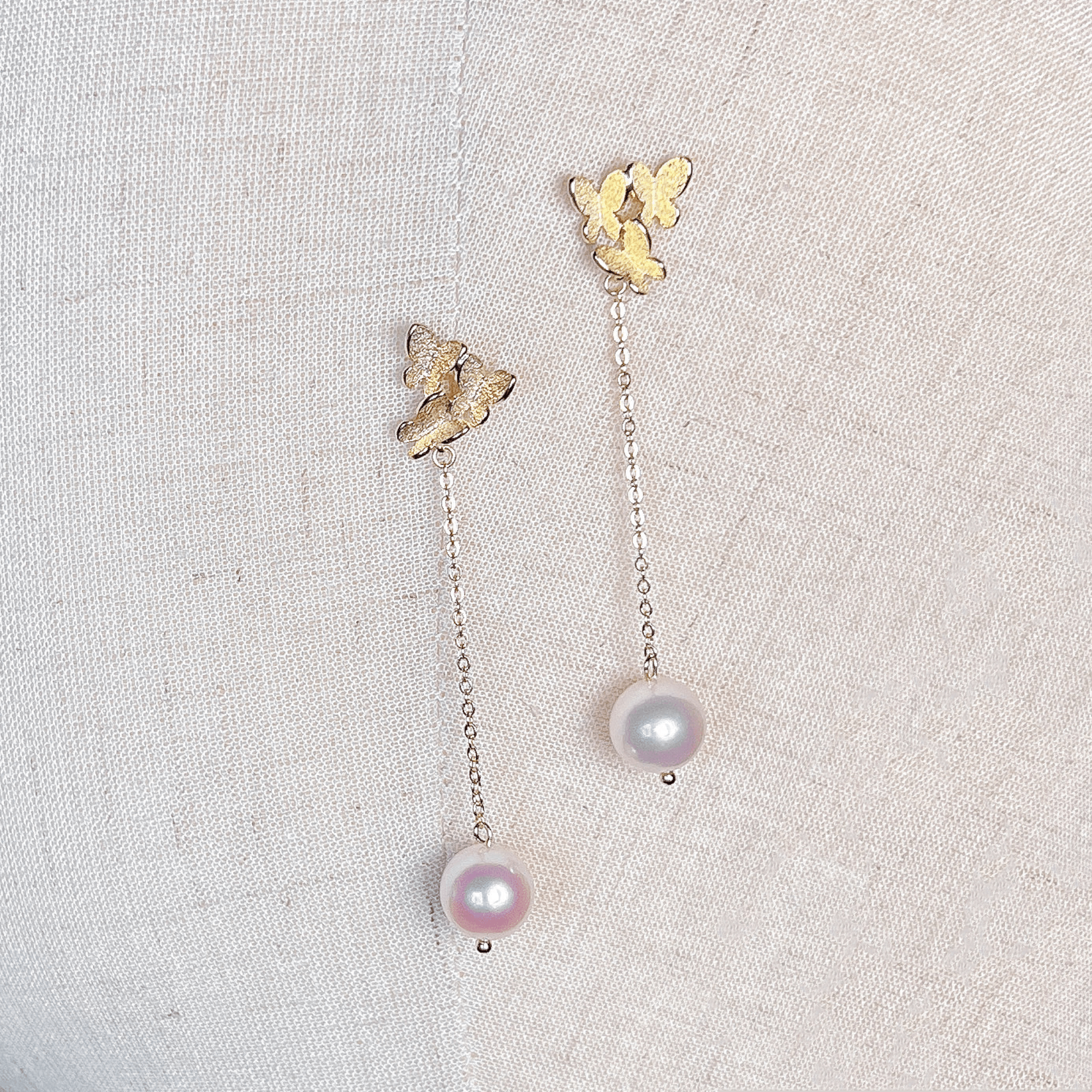 Pair of gold butterfly pearl dangle earrings displayed against a clean white background.