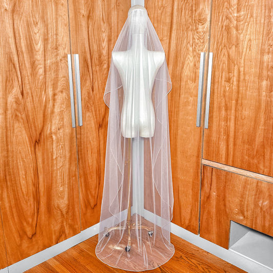 Full-length back view showing the floor-length cascade wedding veil with detailed corded edging.