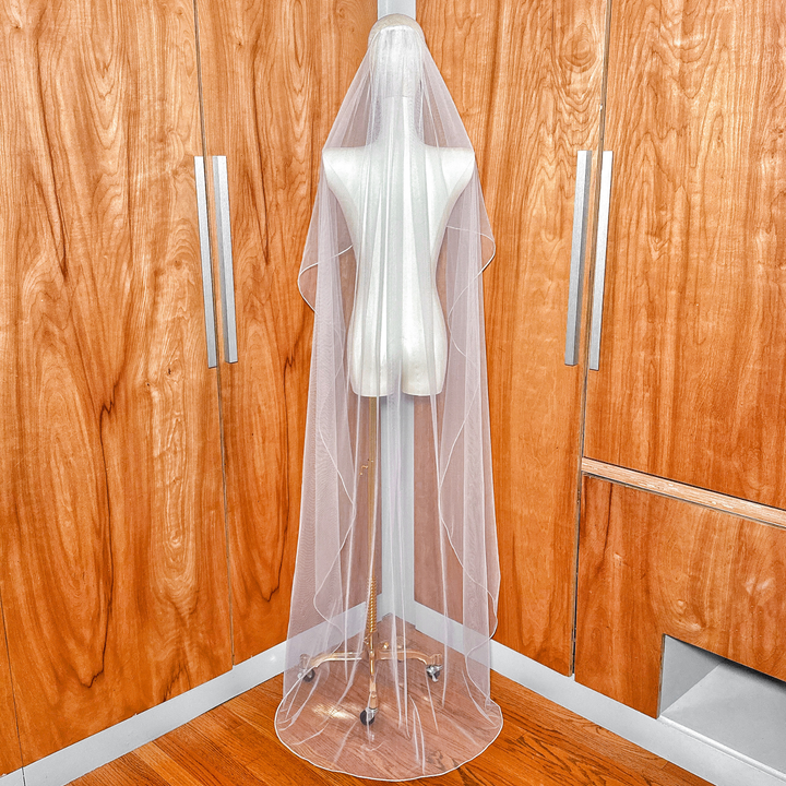 Full-length back view showing the floor-length cascade wedding veil with detailed corded edging.