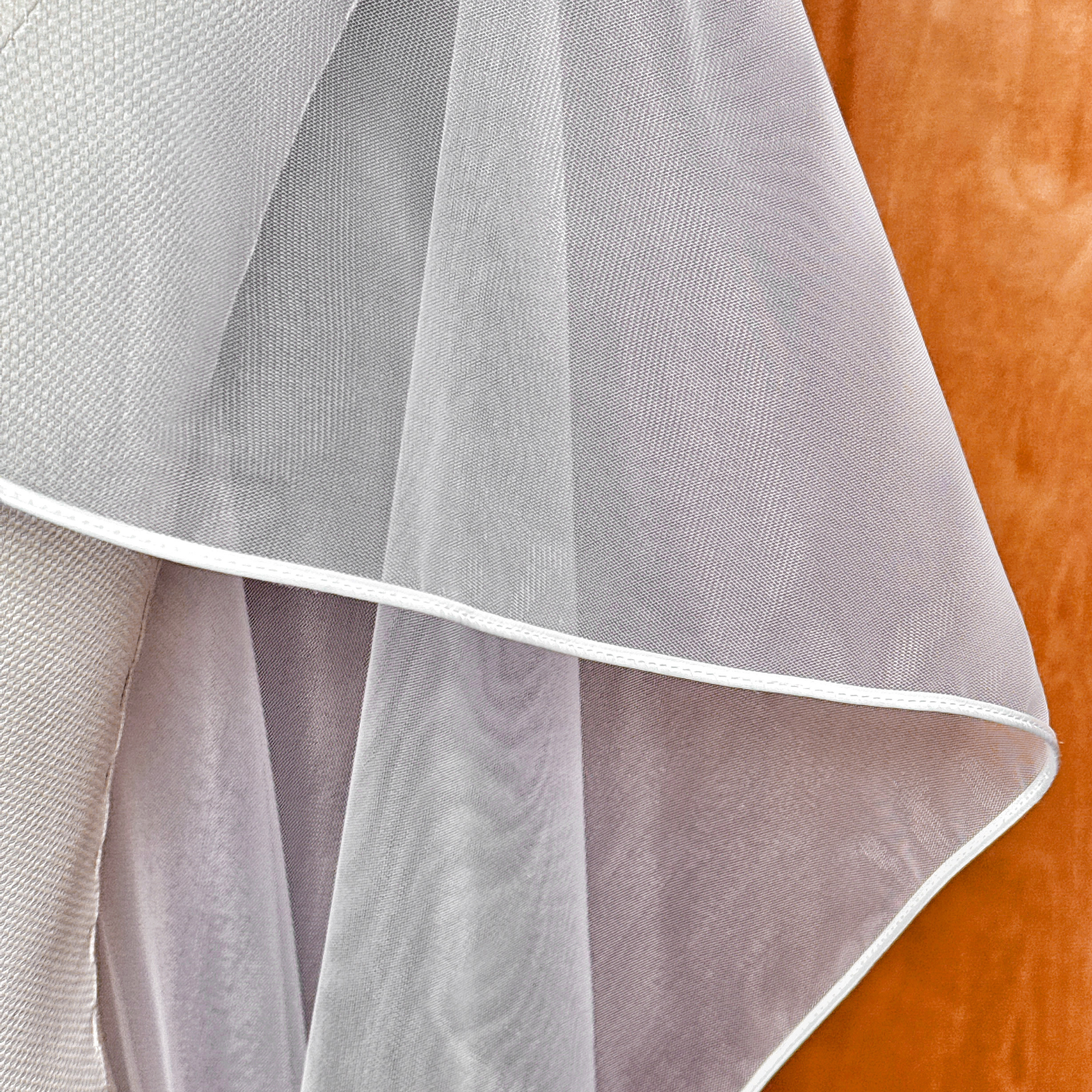 Studio lighting highlighting the soft folds and corded edge border of a floor-length cascade wedding veil.