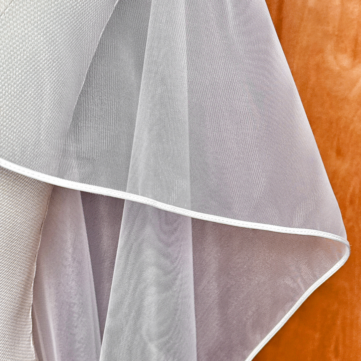 Studio lighting highlighting the soft folds and corded edge border of a floor-length cascade wedding veil.
