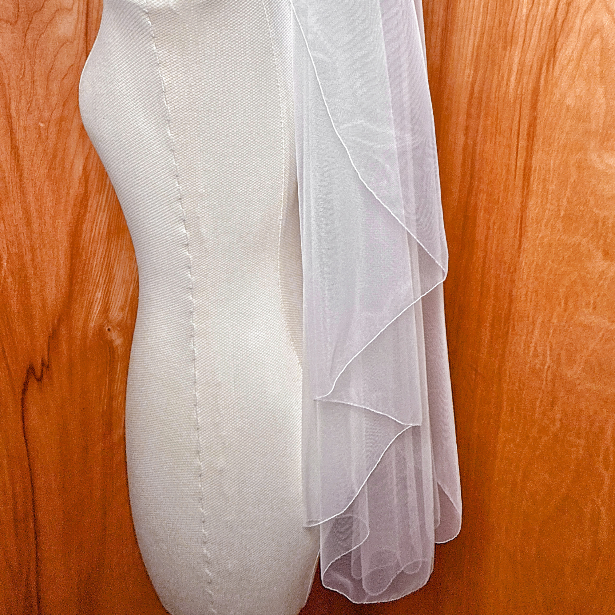 Detail view of a cascade hip length wedding veil with a clean pencil edge displayed on a bridal mannequin.