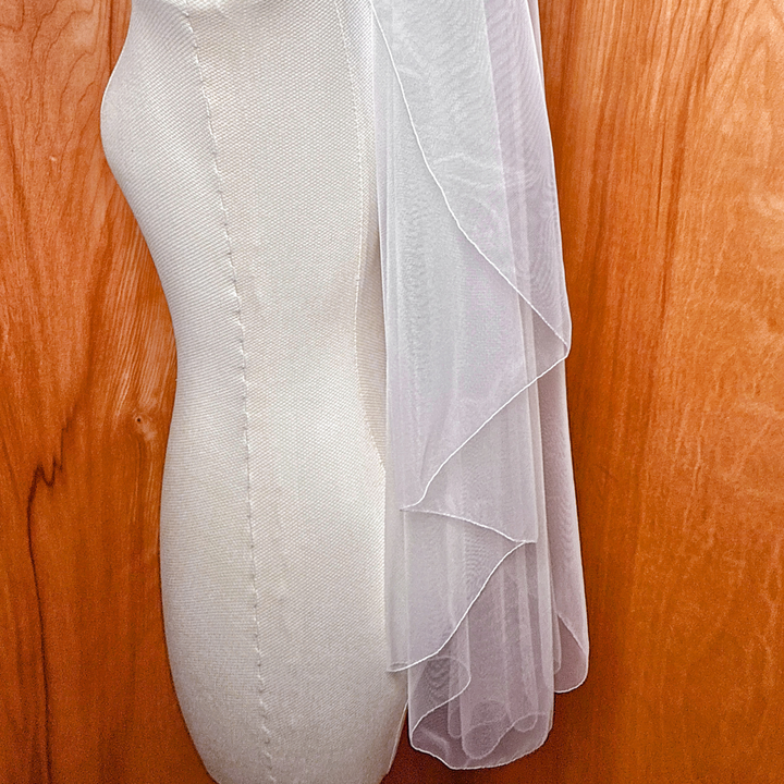 Detail view of a cascade hip length wedding veil with a clean pencil edge displayed on a bridal mannequin.