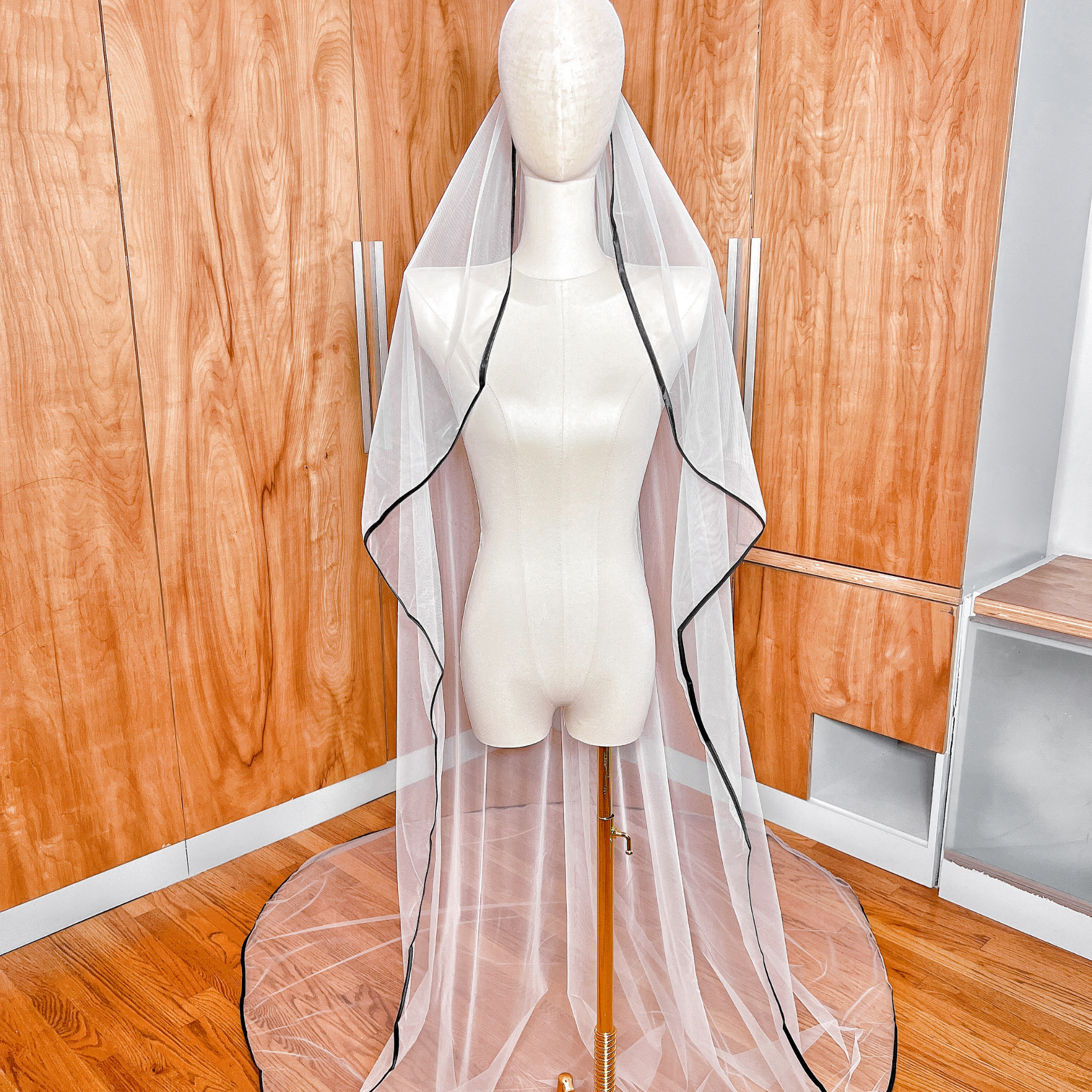 Cathedral length cascade wedding veil with black satin trim draped over a display bust.