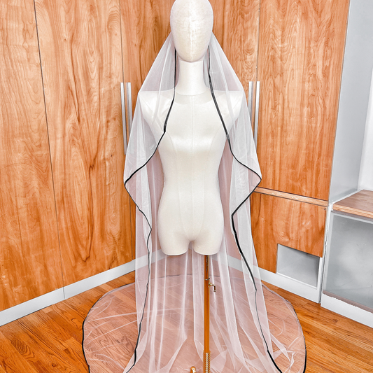 Cathedral length cascade wedding veil with black satin trim draped over a display bust.