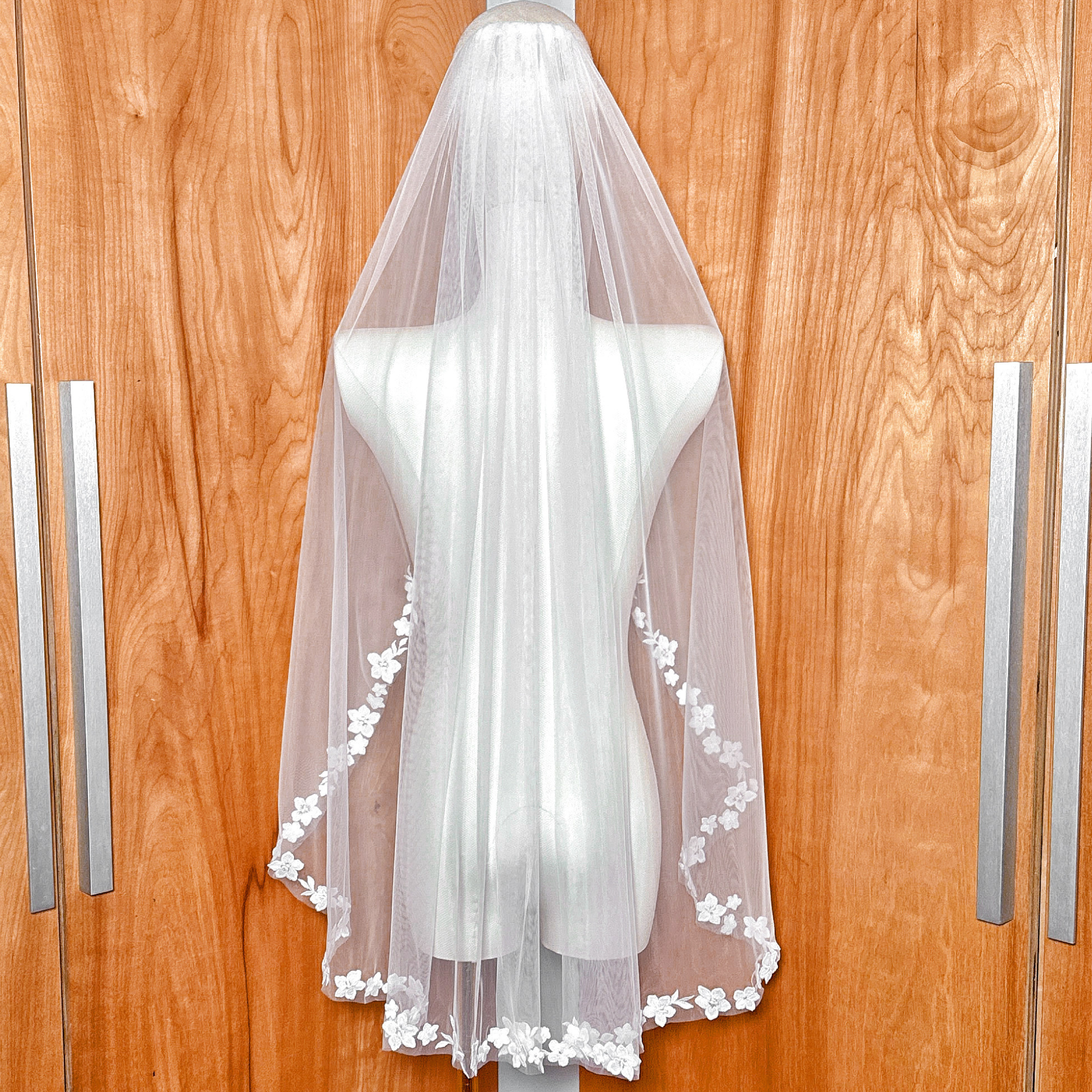 Back view of a fingertip bridal veil featuring intricate cascading floral lace details on a bridal mannequin.