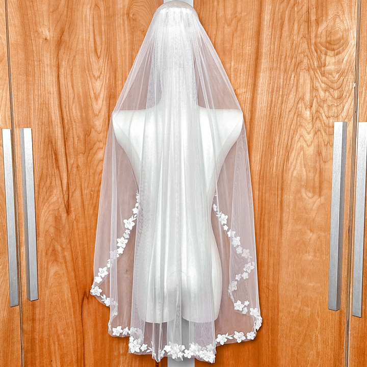Back view of a fingertip bridal veil featuring intricate cascading floral lace details on a bridal mannequin.