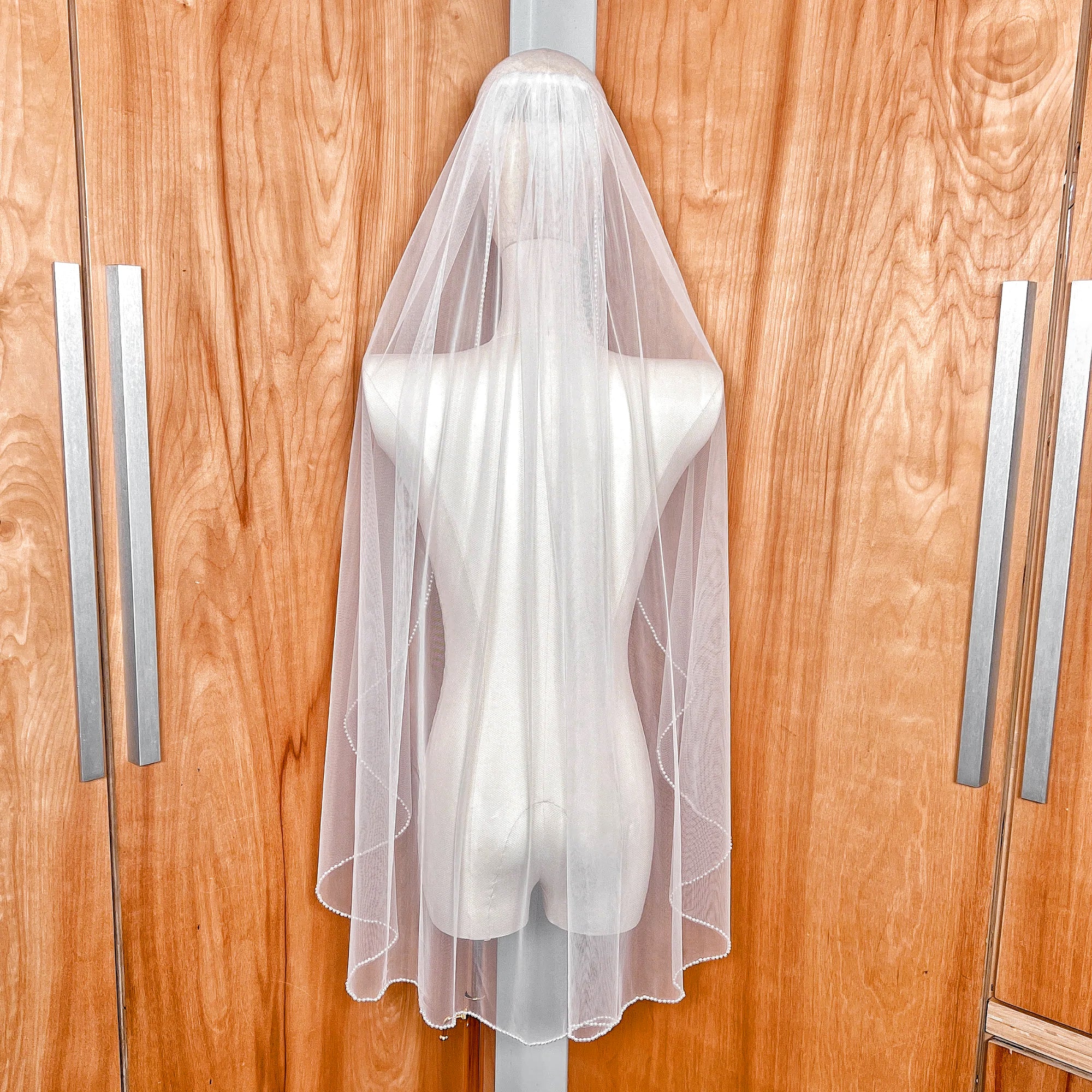 Rear view of the cascading pearl edge wedding veil draped over a mannequin, highlighting the 36-inch fingertip length and pearl detailing.