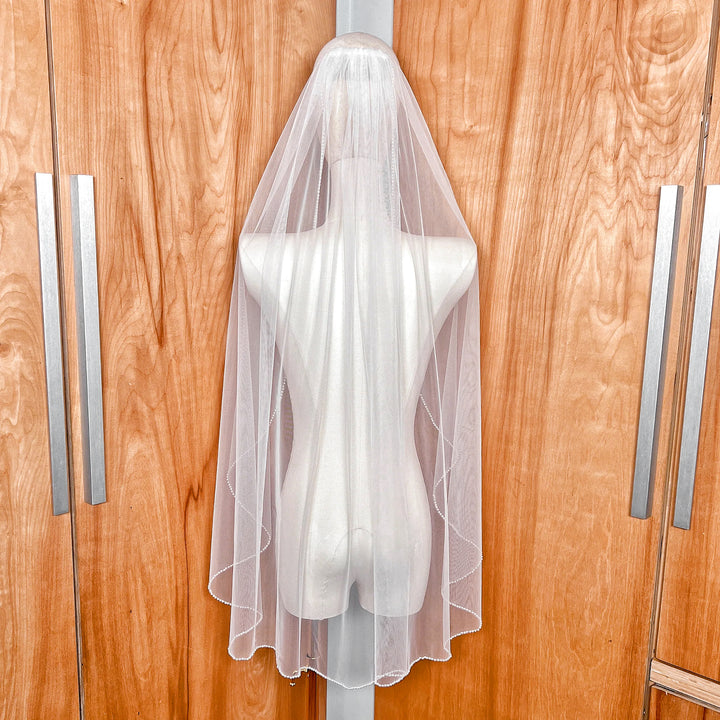 Rear view of the cascading pearl edge wedding veil draped over a mannequin, highlighting the 36-inch fingertip length and pearl detailing.