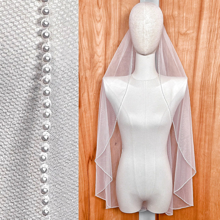 A sheer fingertip length wedding veil with a cascading pearl edge displayed on a bridal mannequin.