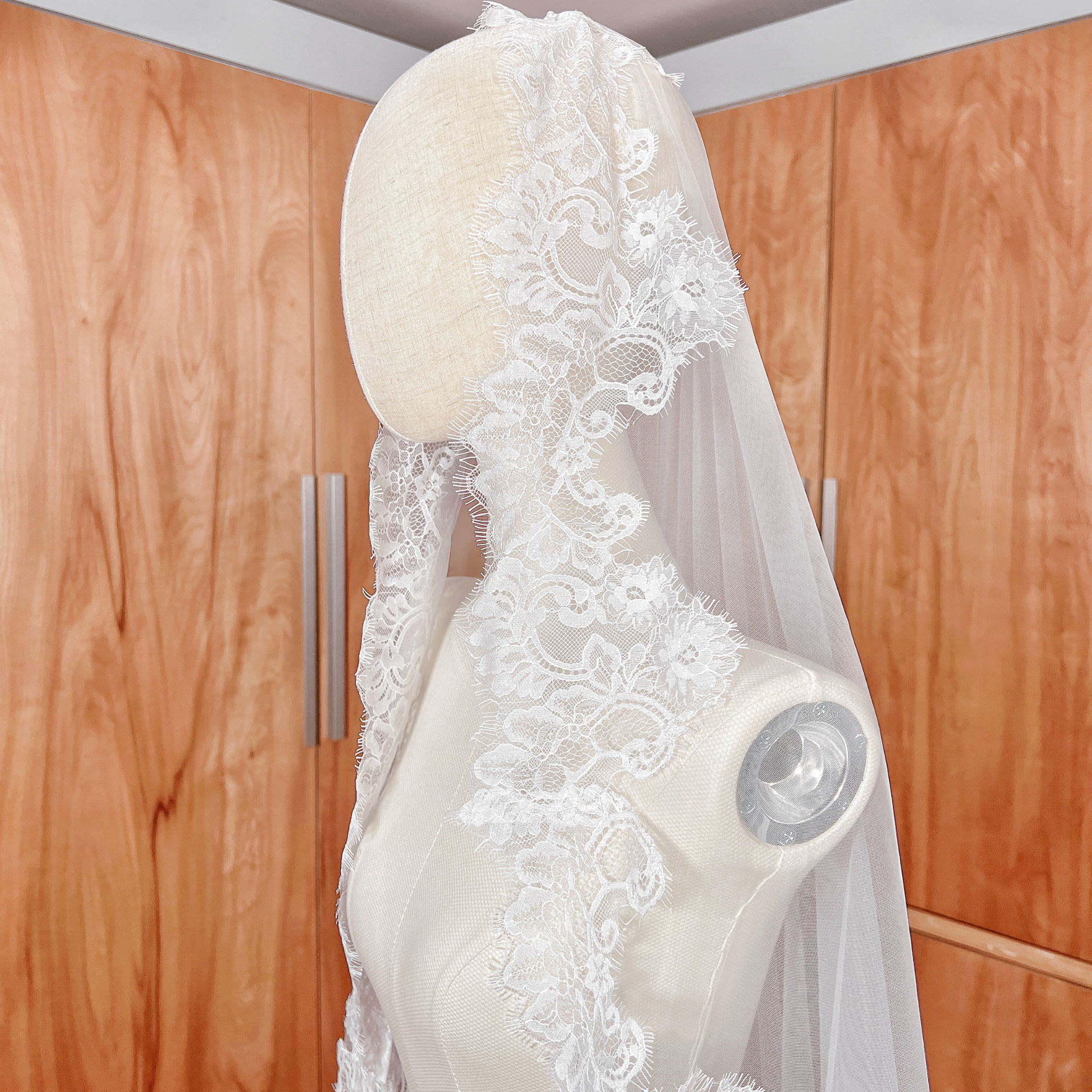 Side profile of a 118-inch cathedral length Chantilly lace bridal mantilla veil on a dress form.