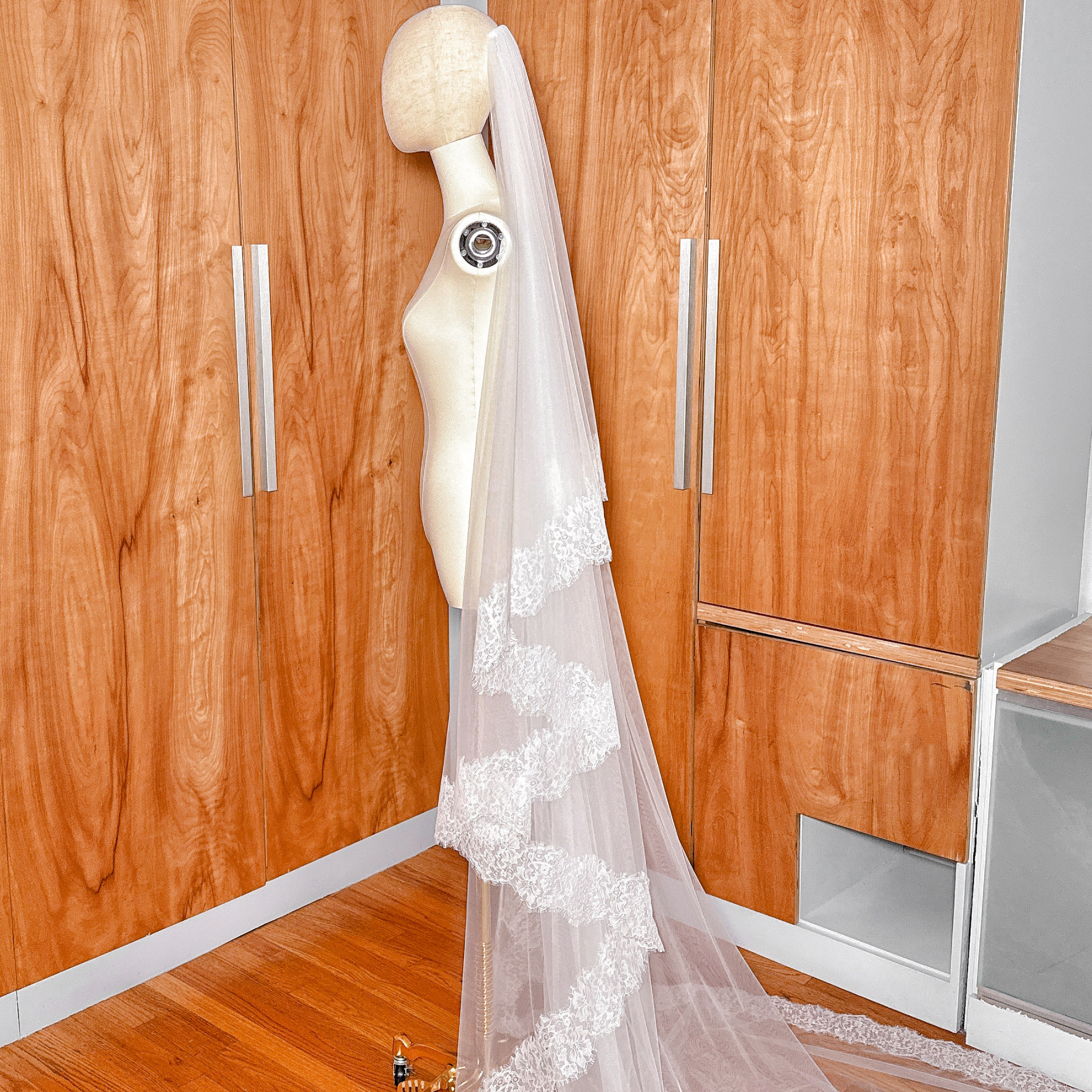 Long cathedral length bridal veil featuring intricate Chantilly lace edging on a mannequin.
