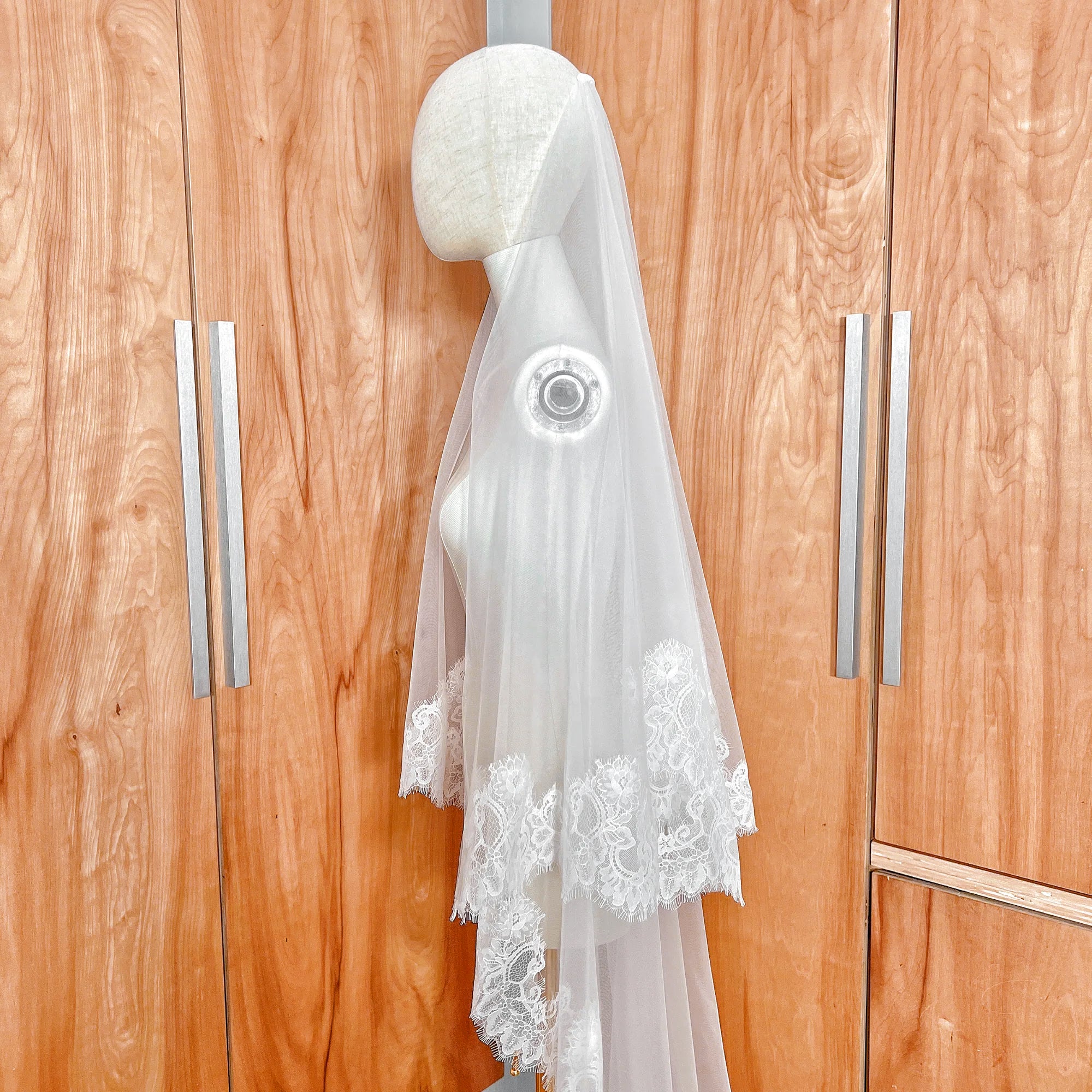 Side profile of a cathedral length Chantilly lace drop wedding veil on a mannequin highlighting the blusher layer.