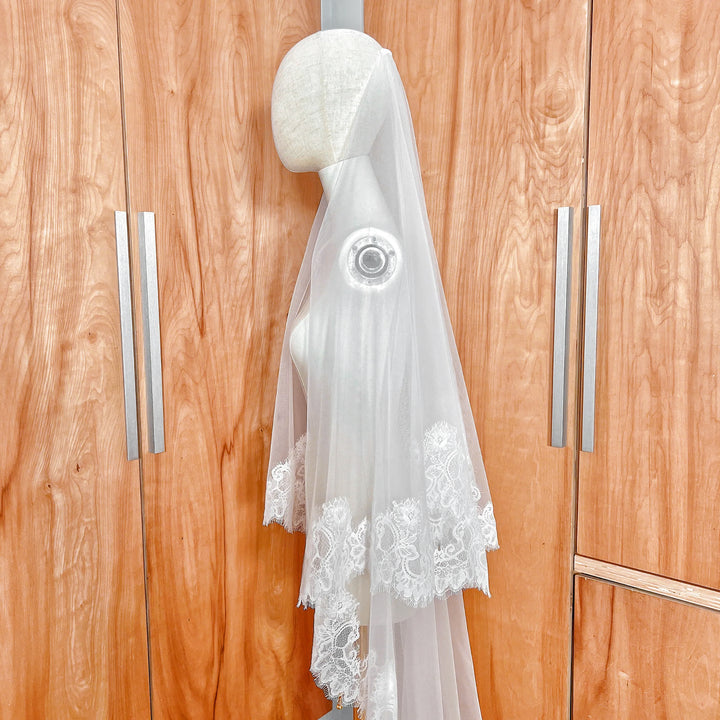Side profile of a cathedral length Chantilly lace drop wedding veil on a mannequin highlighting the blusher layer.