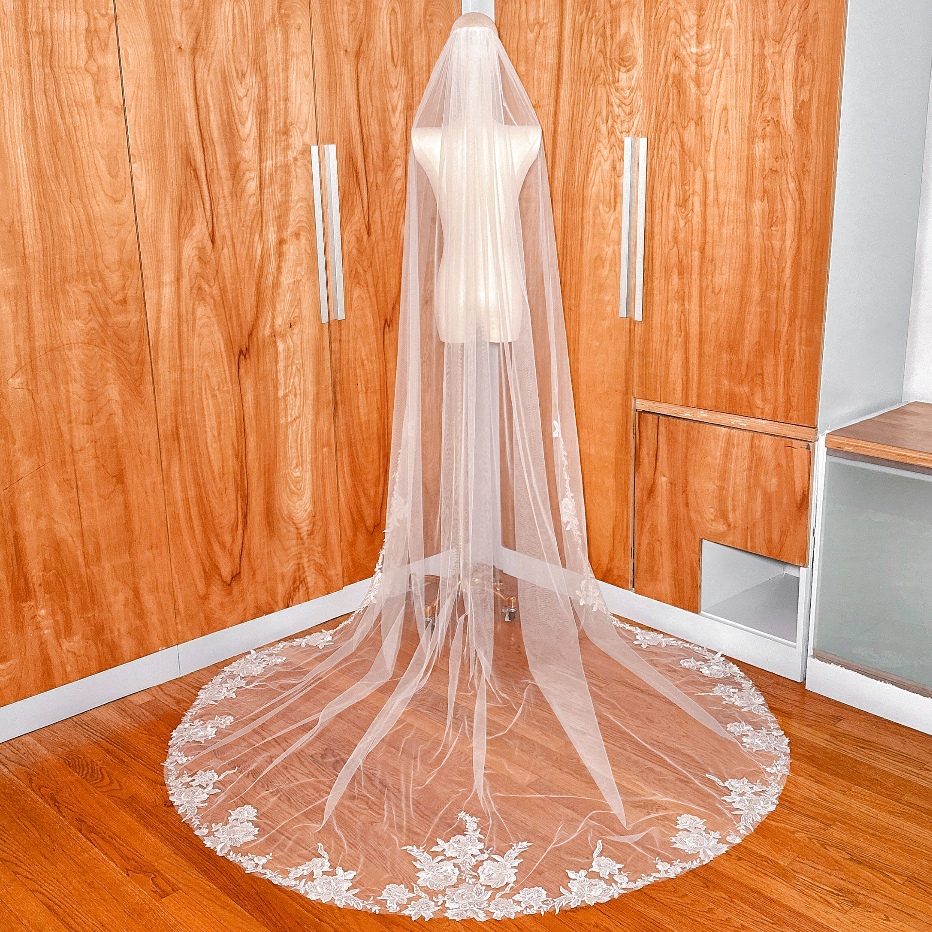 Back view of a cathedral length wedding veil with intricate floral lace edging draped over a mannequin.