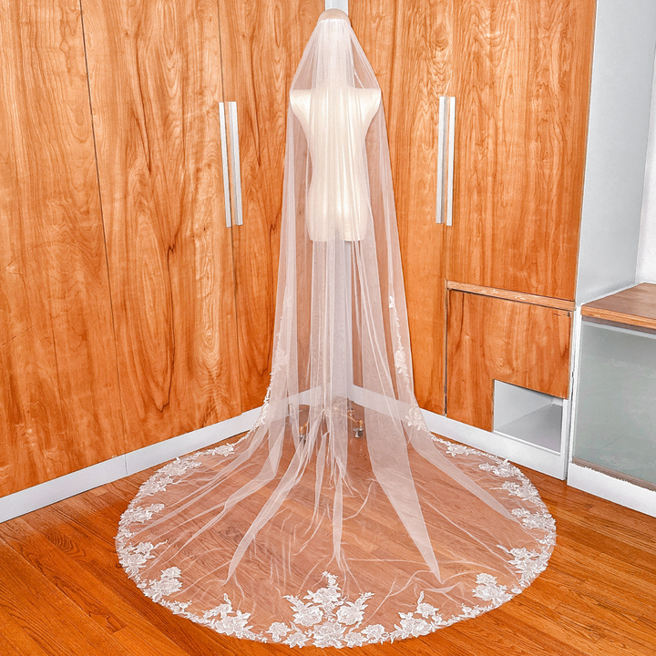 Back view of a cathedral length wedding veil with intricate floral lace edging draped over a mannequin.