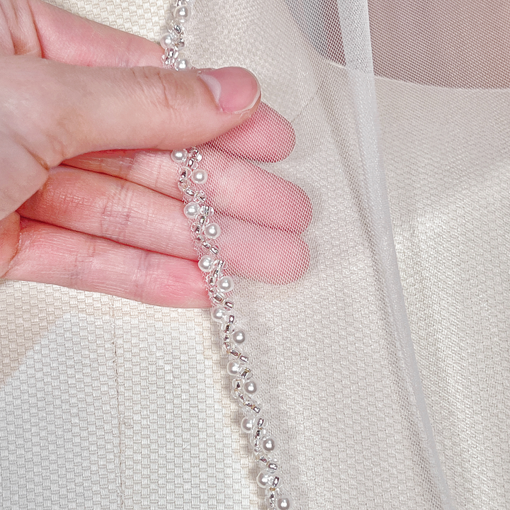 Close-up view of the intricate beaded edge on a soft tulle cathedral wedding veil.