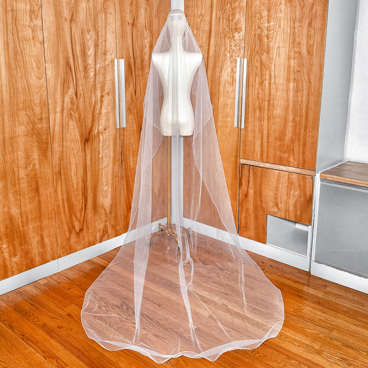 Back view of a cascading bridal veil in cathedral length featuring a delicate 1/8" horsehair edge on a dress form.
