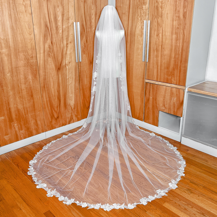 Back view of a cathedral length floral appliqué wedding veil on a mannequin showing the decorative lace edge and train.