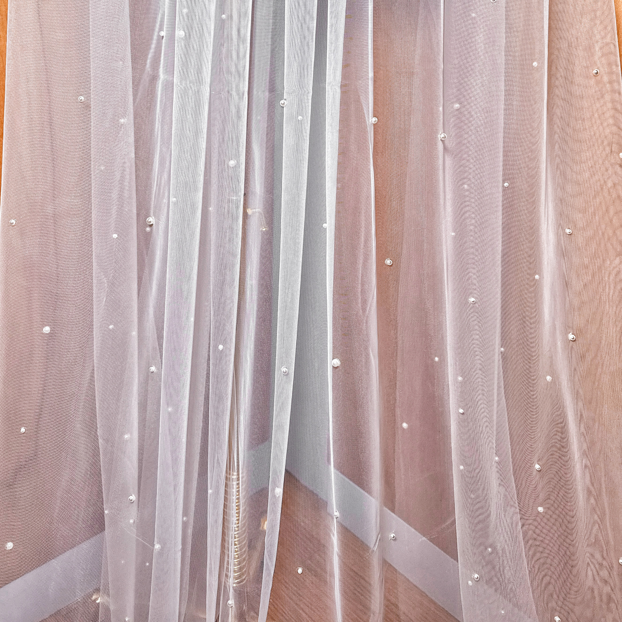 A close-up shot showing the intricate placement of hand-applied pearls on a soft white cathedral bridal veil.