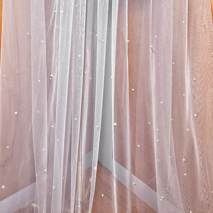 A close-up shot showing the intricate placement of hand-applied pearls on a soft white cathedral bridal veil.